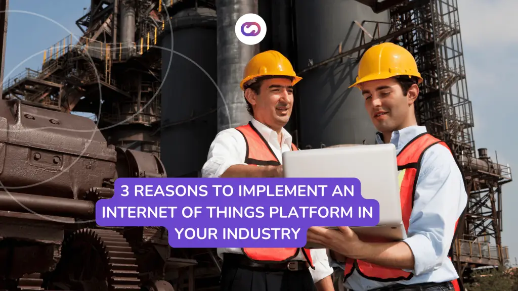 Two industrial workers wearing helmets and safety vests reviewing data on a laptop in front of heavy machinery, representing the implementation of IoT platforms in industrial settings.