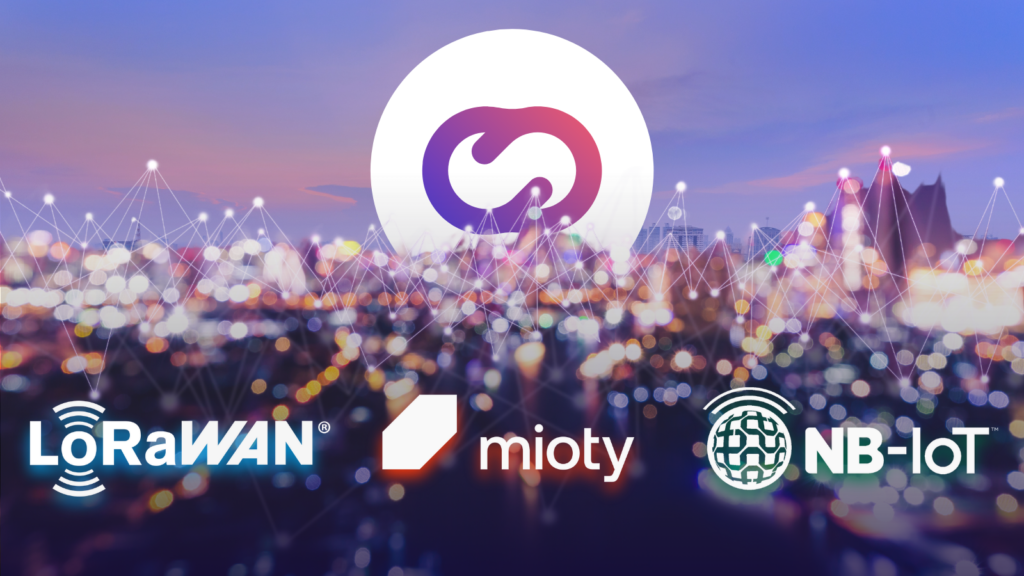 Imagen de ciudad desenfocada con el logo de Cloud Studio y los logotipos de LoRaWAN, mioty y NB-IoT, representando la comparación entre distintas tecnologías inalámbricas para IoT.