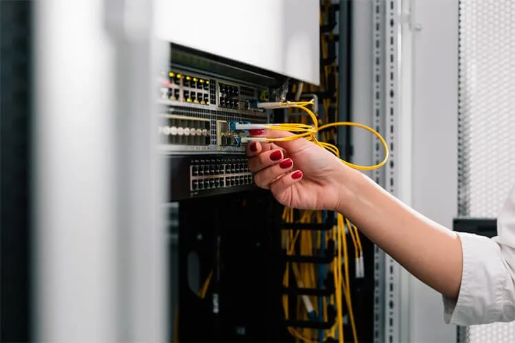 La imagen muestra una mano conectando un cable de Ethernet naranja hacia un servidor de Instancia Privada de Cloud Studio IoT